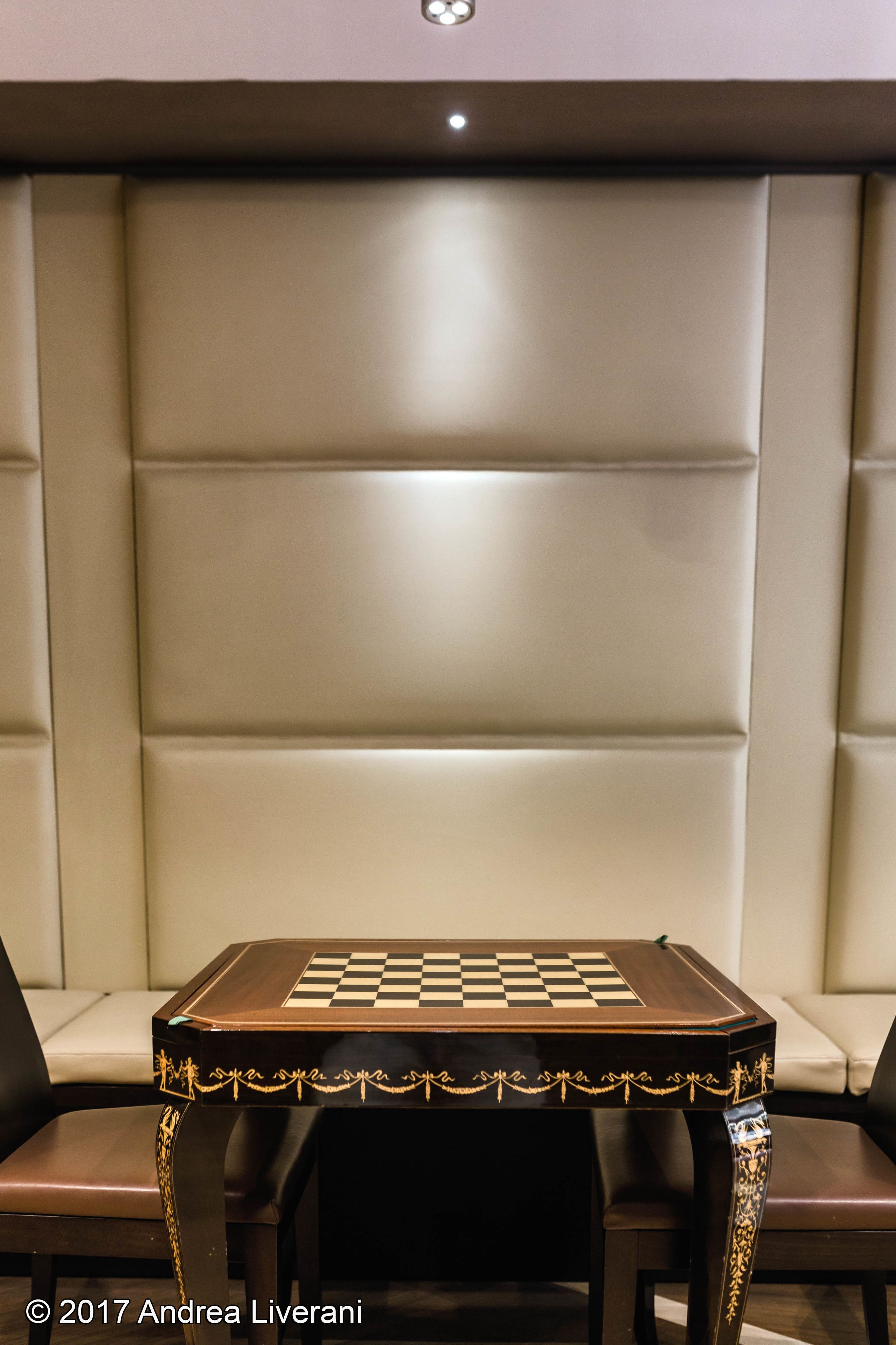 Un tablero de juego a cuadros sobre una mesa con detalles dorados ornamentales, frente a una pared acolchada.