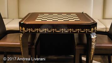 Un tablero de juego a cuadros sobre una mesa con detalles dorados ornamentales, frente a una pared acolchada.