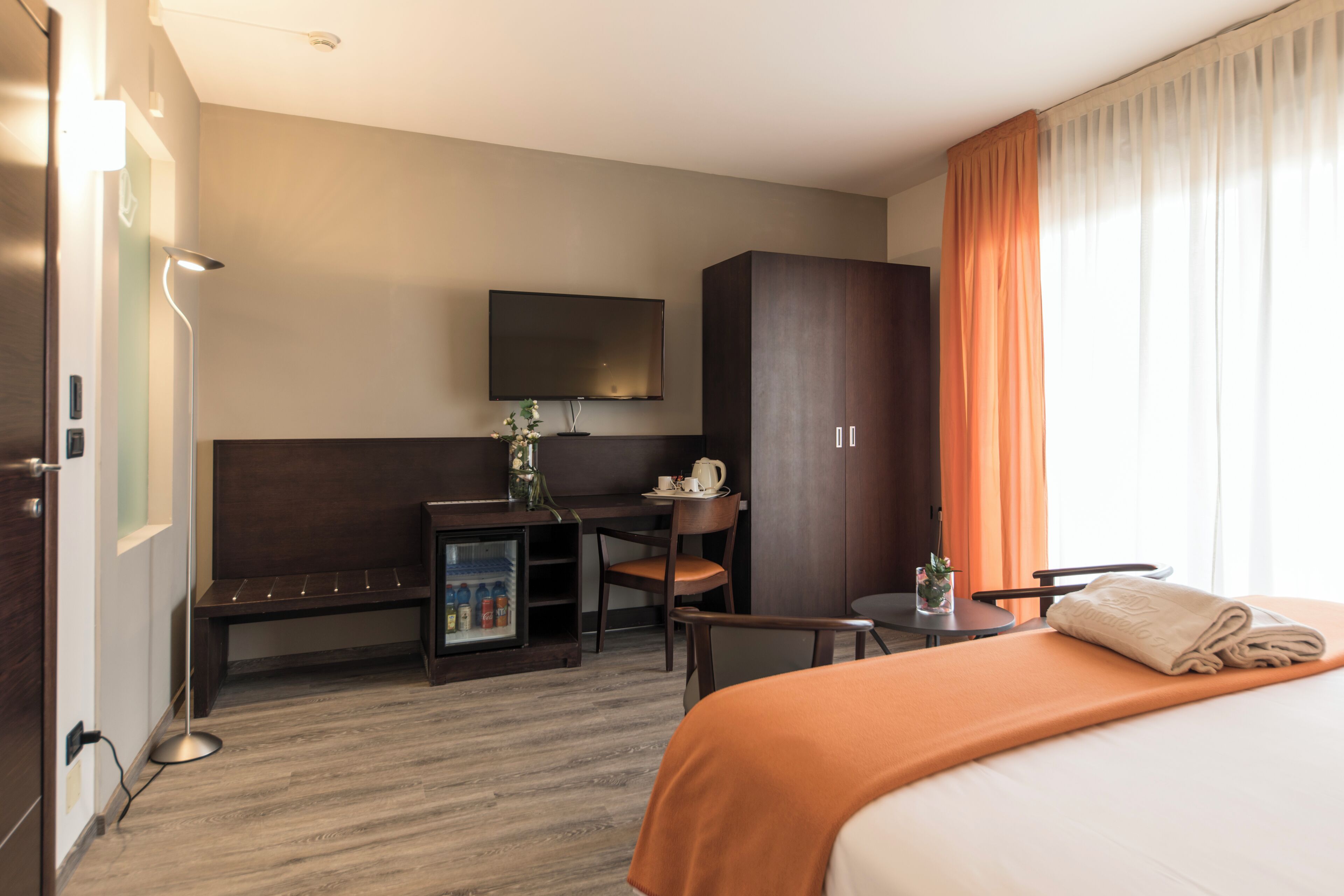 Una camera d'albergo con un letto, una scrivania, una sedia, una televisione e un frigobar.