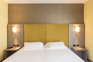 Una habitación de hotel con una cama grande, dos mesitas de noche y lámparas de pared.