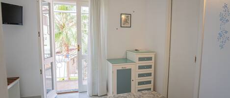 A bedroom with a bed, a desk, a chair, a TV, and a door leading to a balcony.