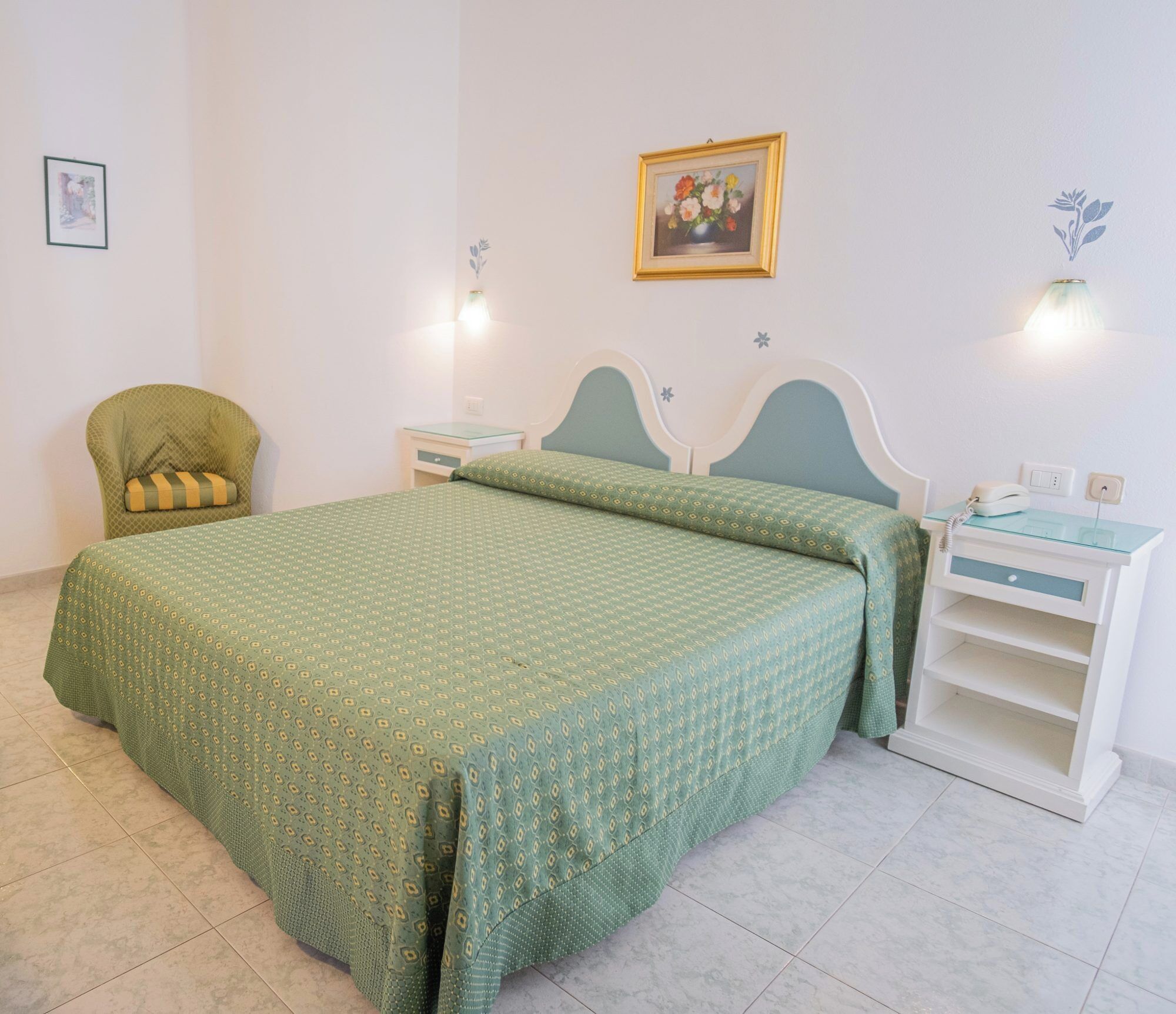 Un dormitorio ordenado con cama, sillón, mesita de noche y tocador.