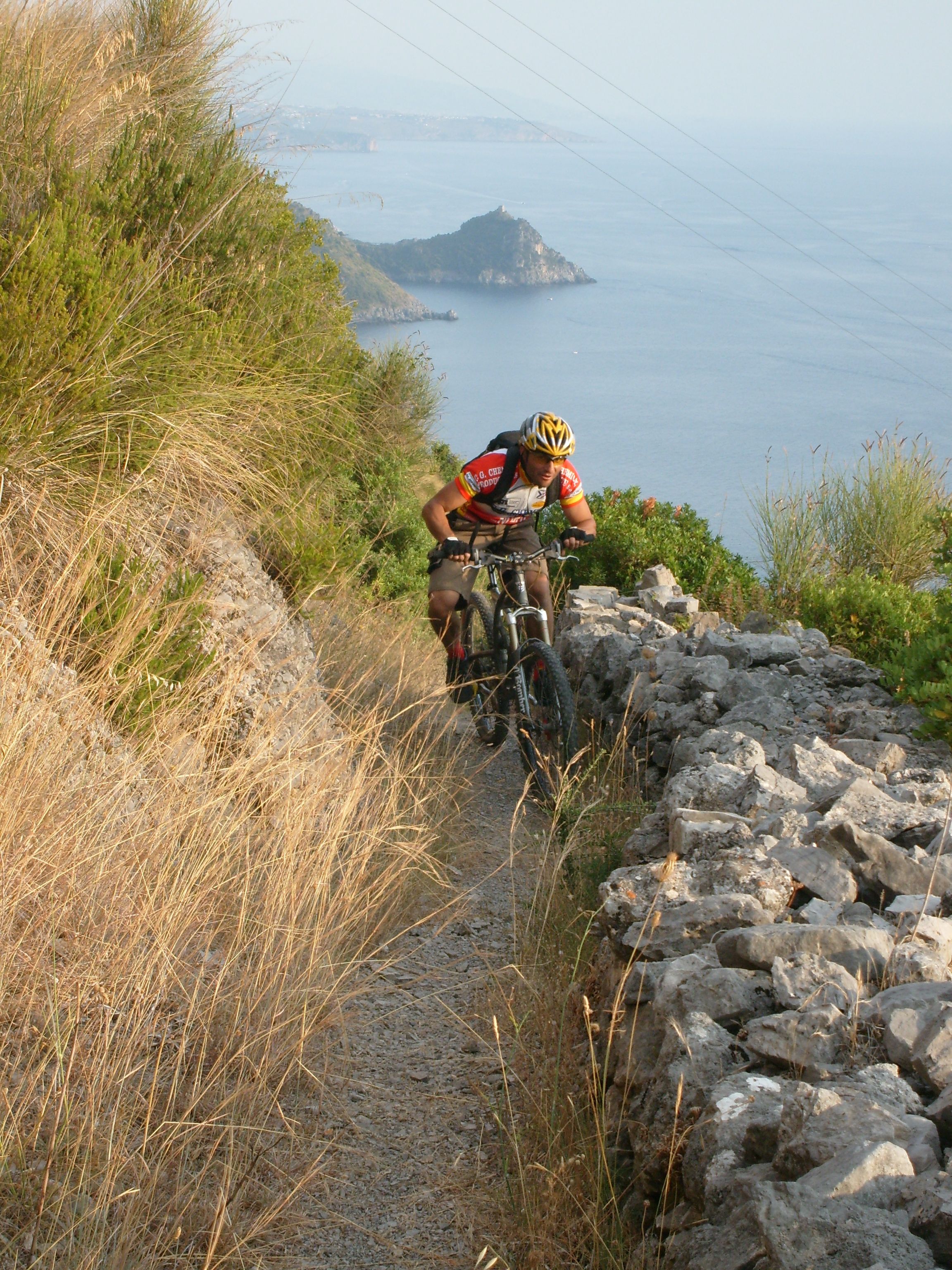 A mountain biker on a rocky trail with a view of the sea and distant islands.