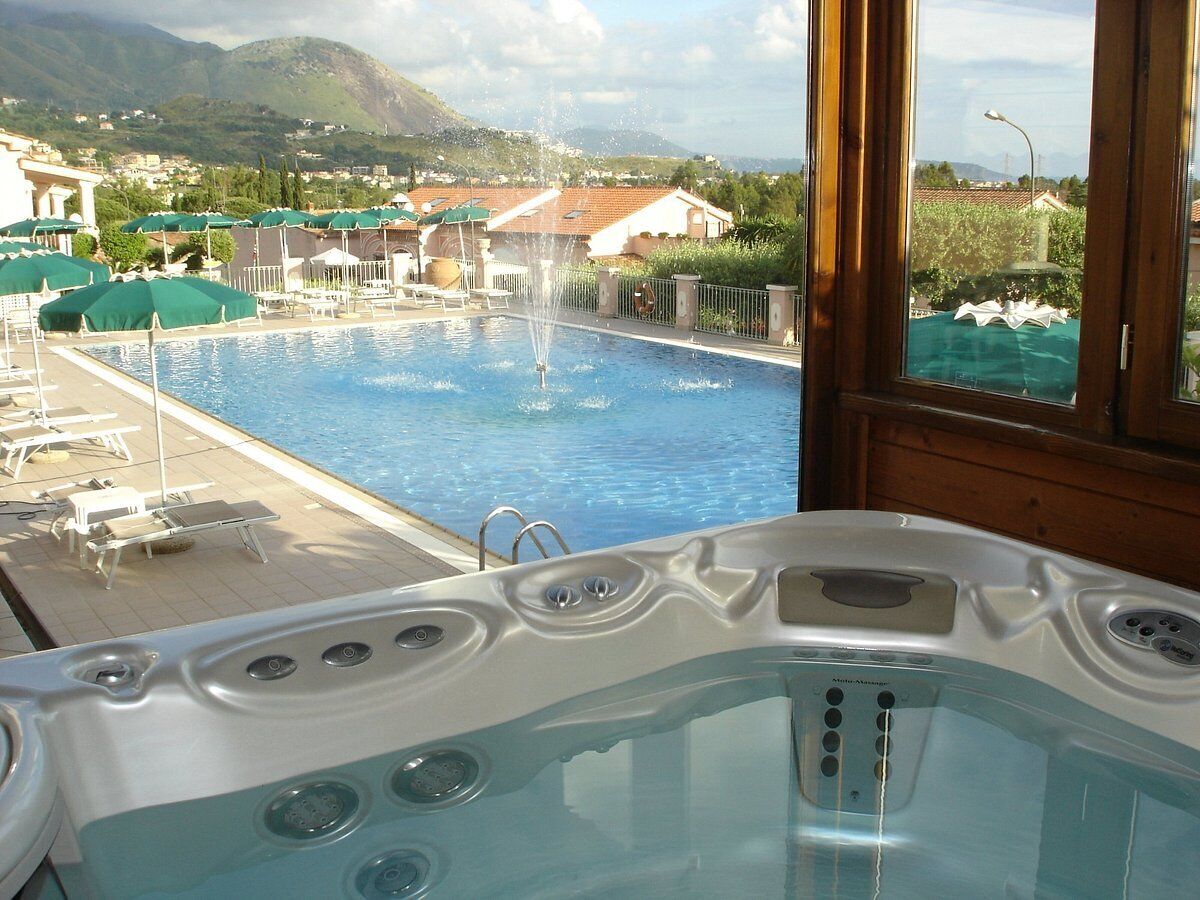 A hot tub with a view of a swimming pool and mountains in the background.