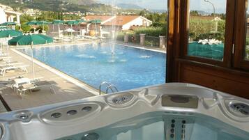 A hot tub with a view of a swimming pool and mountains in the background.
