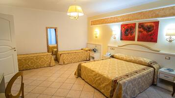 Una camera d'albergo con due letti singoli, un letto matrimoniale, una sedia, un comodino con una lampada e un'opera d'arte appesa al muro.