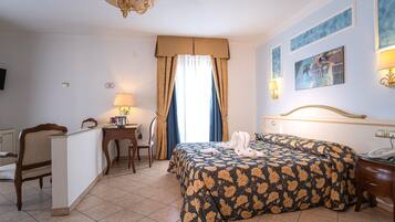 Una habitación de hotel con cama, escritorio, silla, lámpara y obras de arte en las paredes.