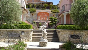 Uma estátua em um pátio com bancos de pedra, uma escadaria de pedra e um edifício com sacadas e uma placa com a inscrição "Borgo La Tana".
