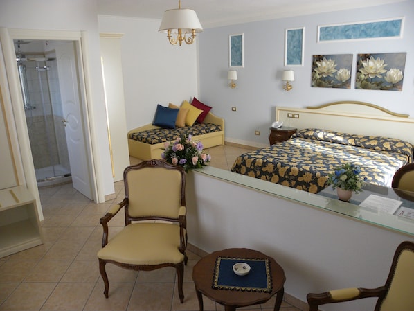 A hotel room with a bed, a chair, a small table, a desk, a shower, and a mirror.