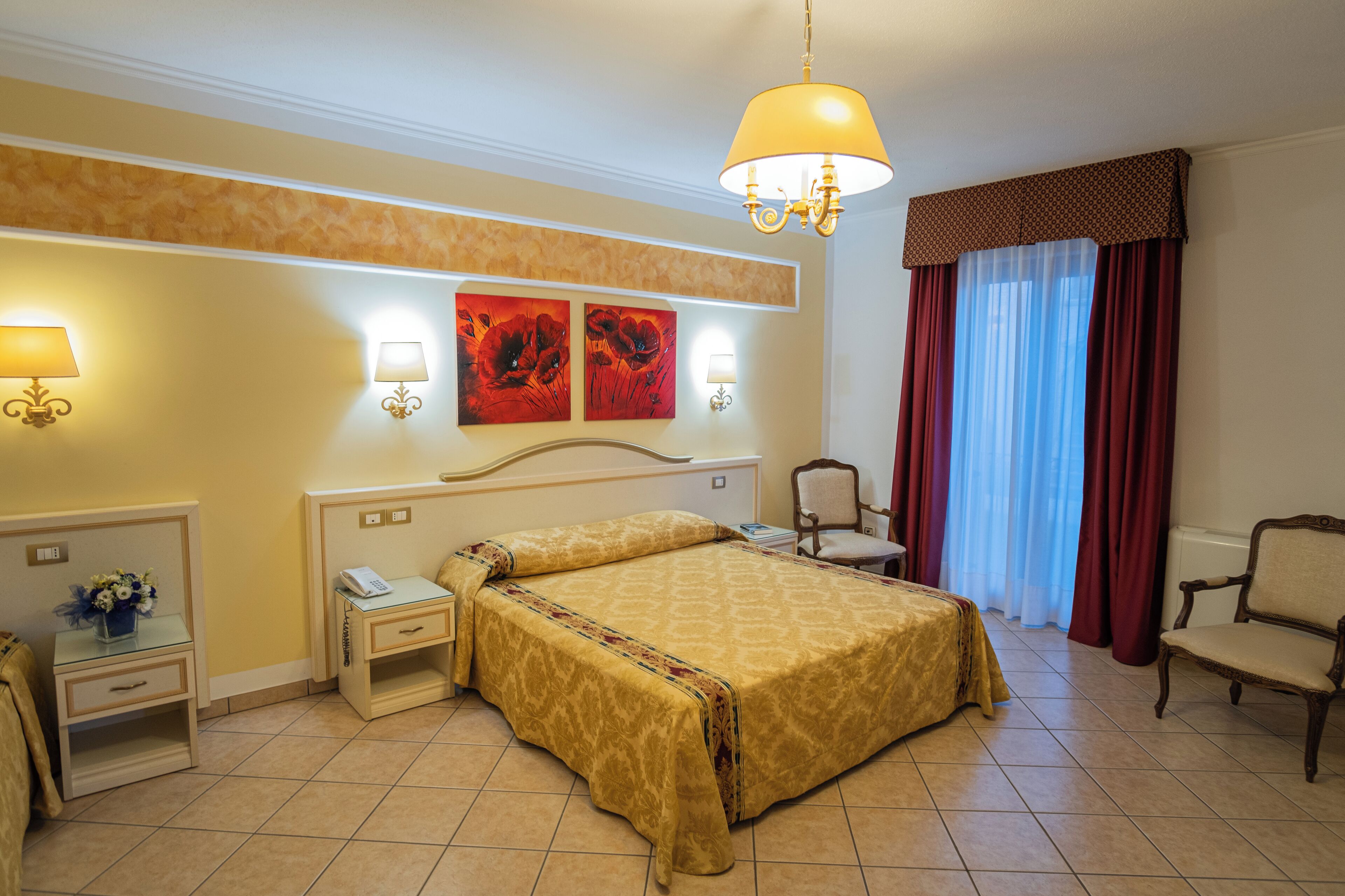 Habitación de hotel con cama, mesitas de noche, lámparas, una silla y obras de arte en la pared.