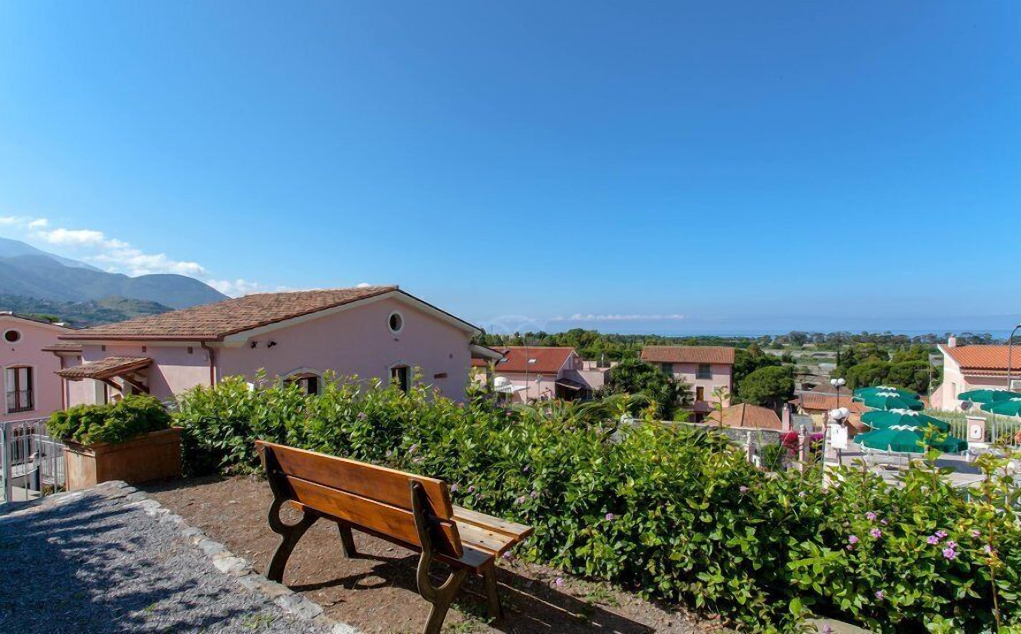 A bench in a garden area with a view of a pink building and surrounding houses.