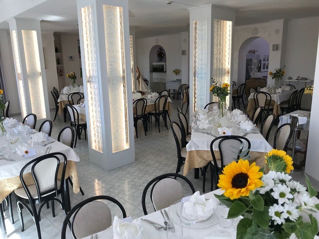 A restaurant with multiple tables set for dining, featuring white tablecloths and sunflowers.