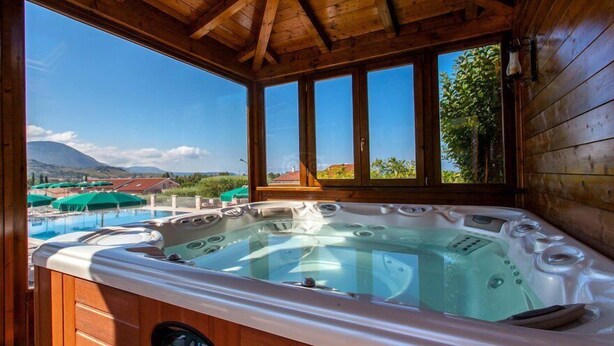 Uma cabana de madeira com hidromassagem e vista para uma piscina e montanhas.