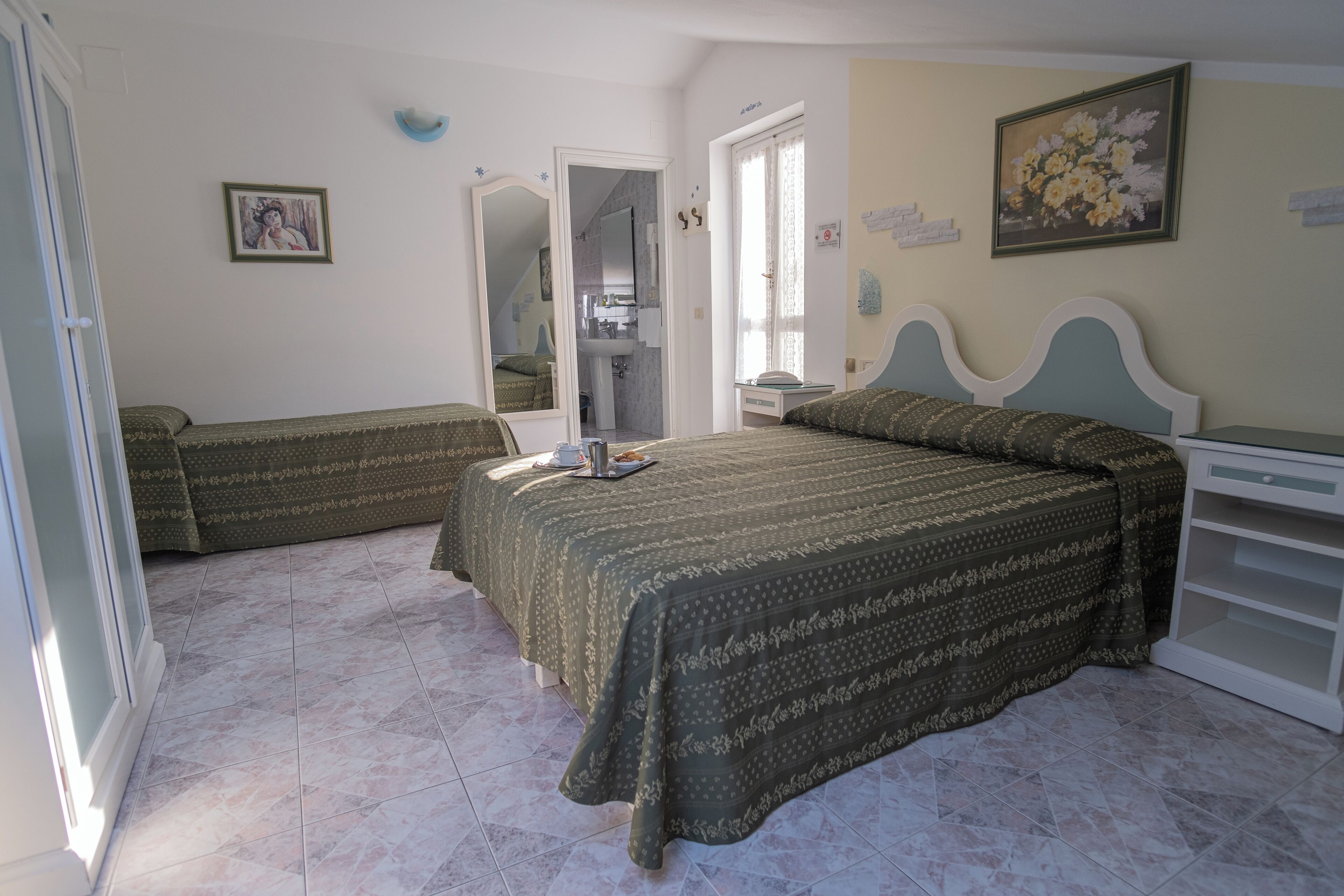 A bedroom with two beds, a wardrobe, a bedside table, and a bathroom visible through an open door.