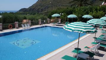 Ein Swimmingpool mit Liegestühlen und Sonnenschirmen, umgeben von Grünpflanzen und einer Bergkulisse.