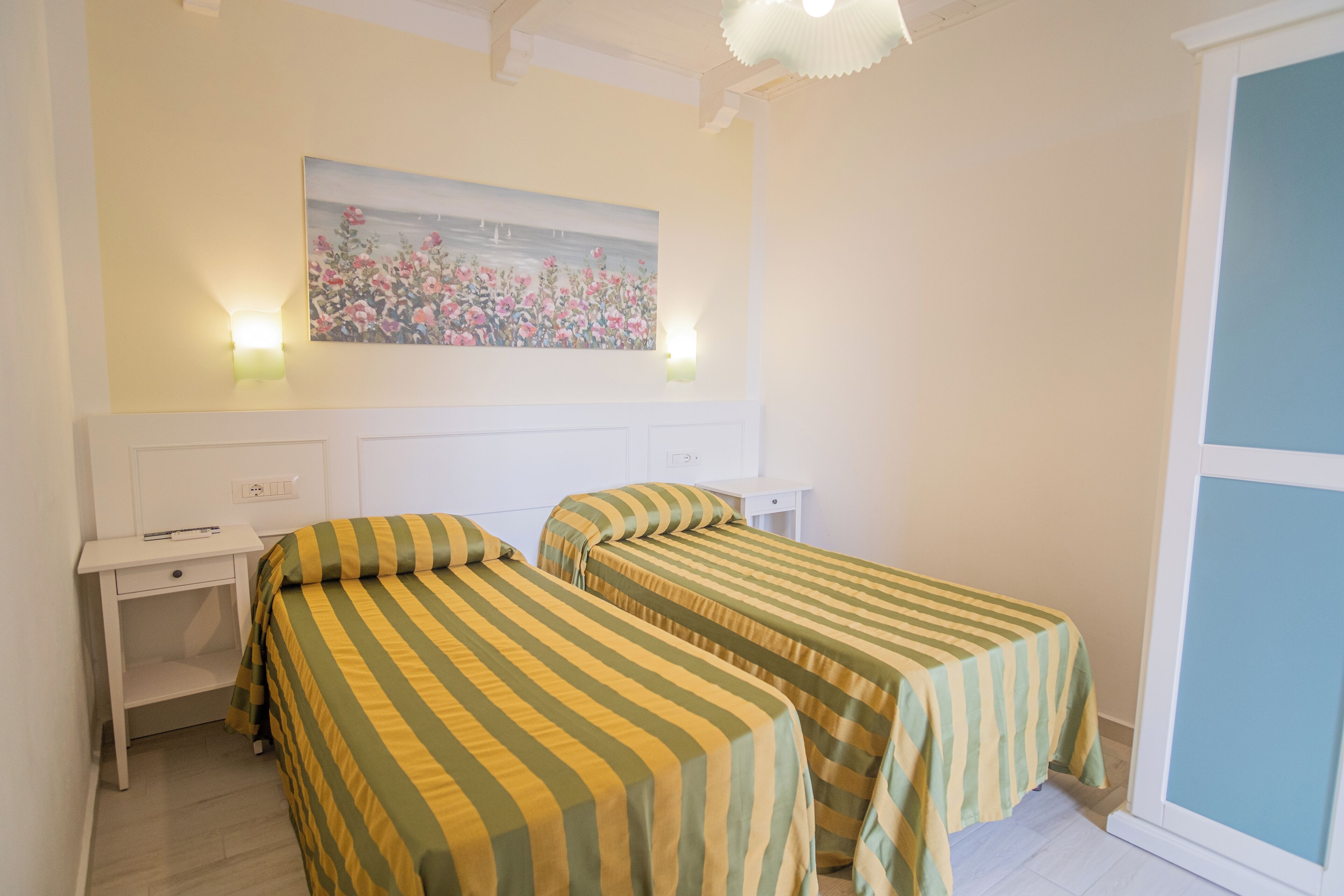 A bedroom with two beds, a nightstand, a desk, and a wall-mounted painting.