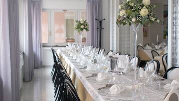 A long dining table set with white tablecloths, silverware, and clear glassware, flanked by black chairs.