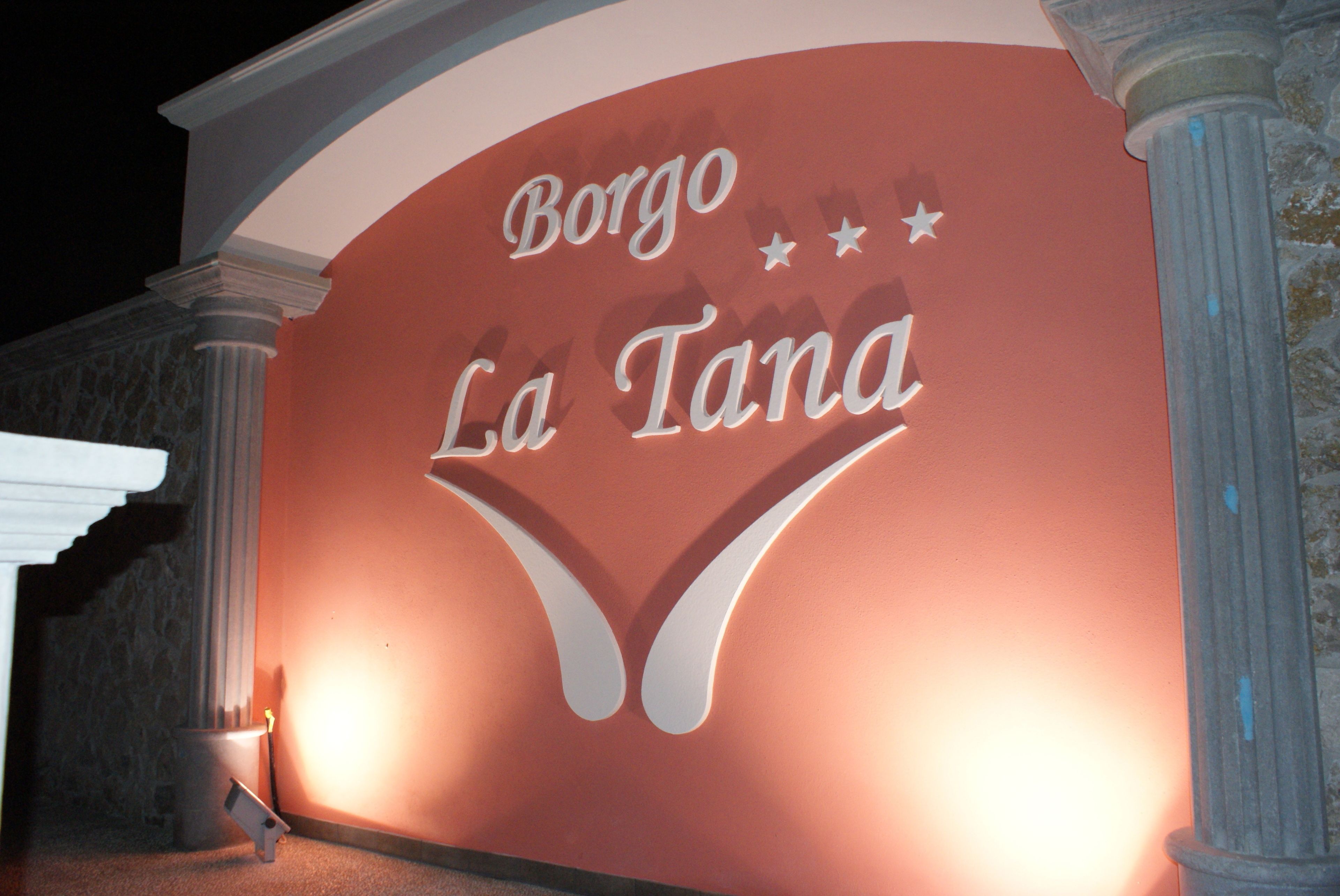 A building facade with the text "Borgo La Tana" illuminated.