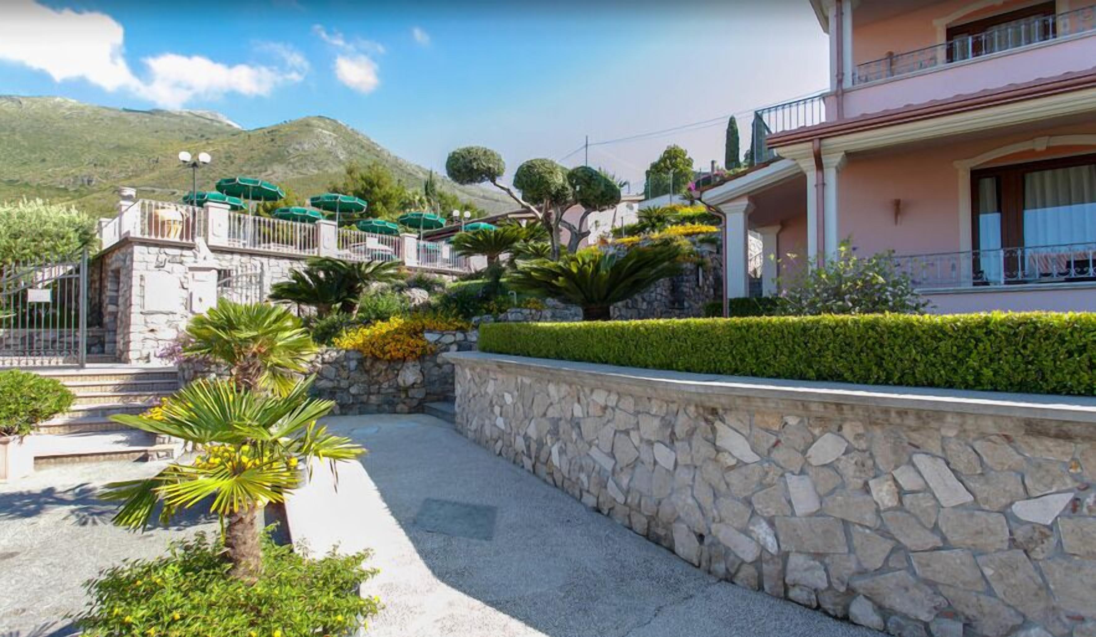 A hotel with a stone wall, a pool, and a mountain backdrop.