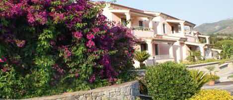 A two-story building with a stone retaining wall and a variety of flowering plants.