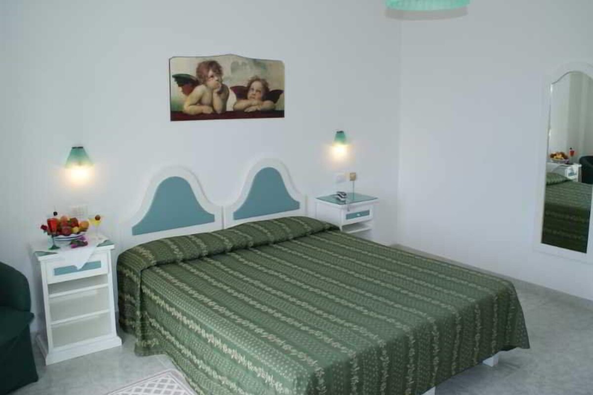 A bedroom with a bed, two bedside tables, a nightstand, a wall-mounted lamp, and a painting.