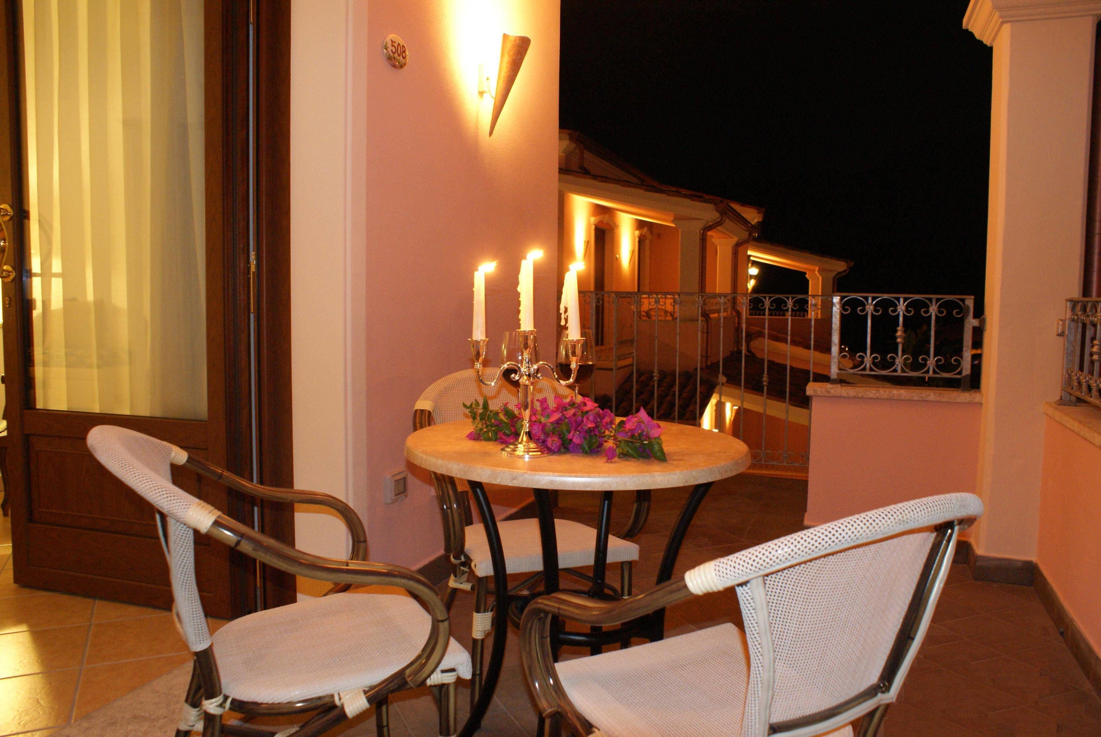 Un balcone con un tavolo apparecchiato per due, con sedie in vimini e candele.