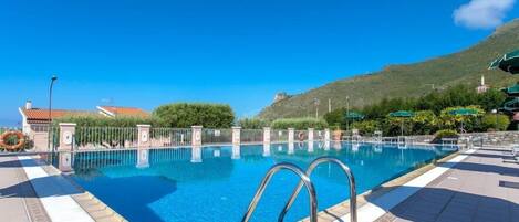 A clear blue pool with a metal ladder, surrounded by a tiled deck and a fence.