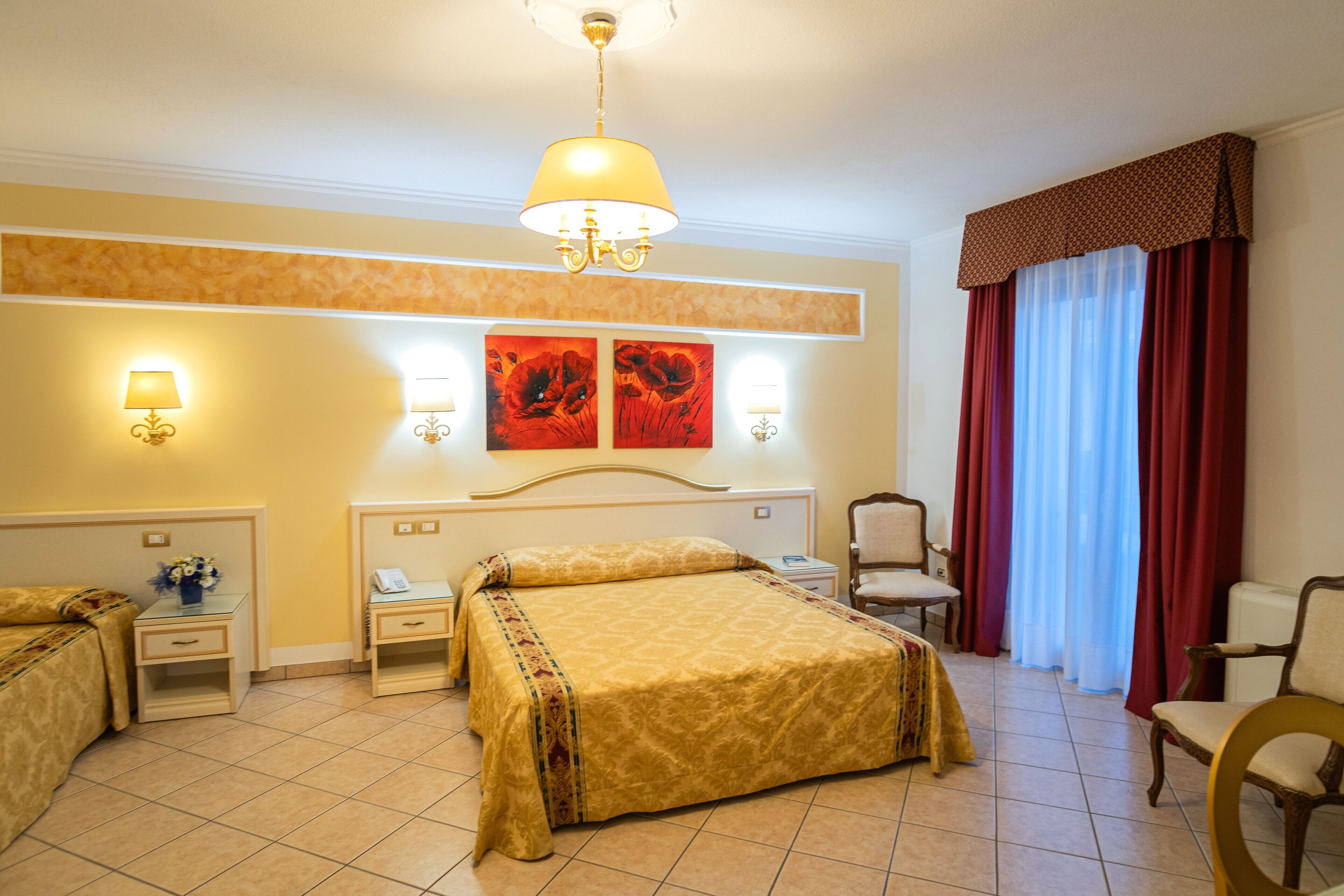 Habitación de hotel con cama, dos mesitas de noche, una silla, un escritorio y un ventanal con cortinas.