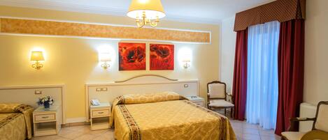 Habitación de hotel con cama, dos mesitas de noche, una silla, un escritorio y un ventanal con cortinas.