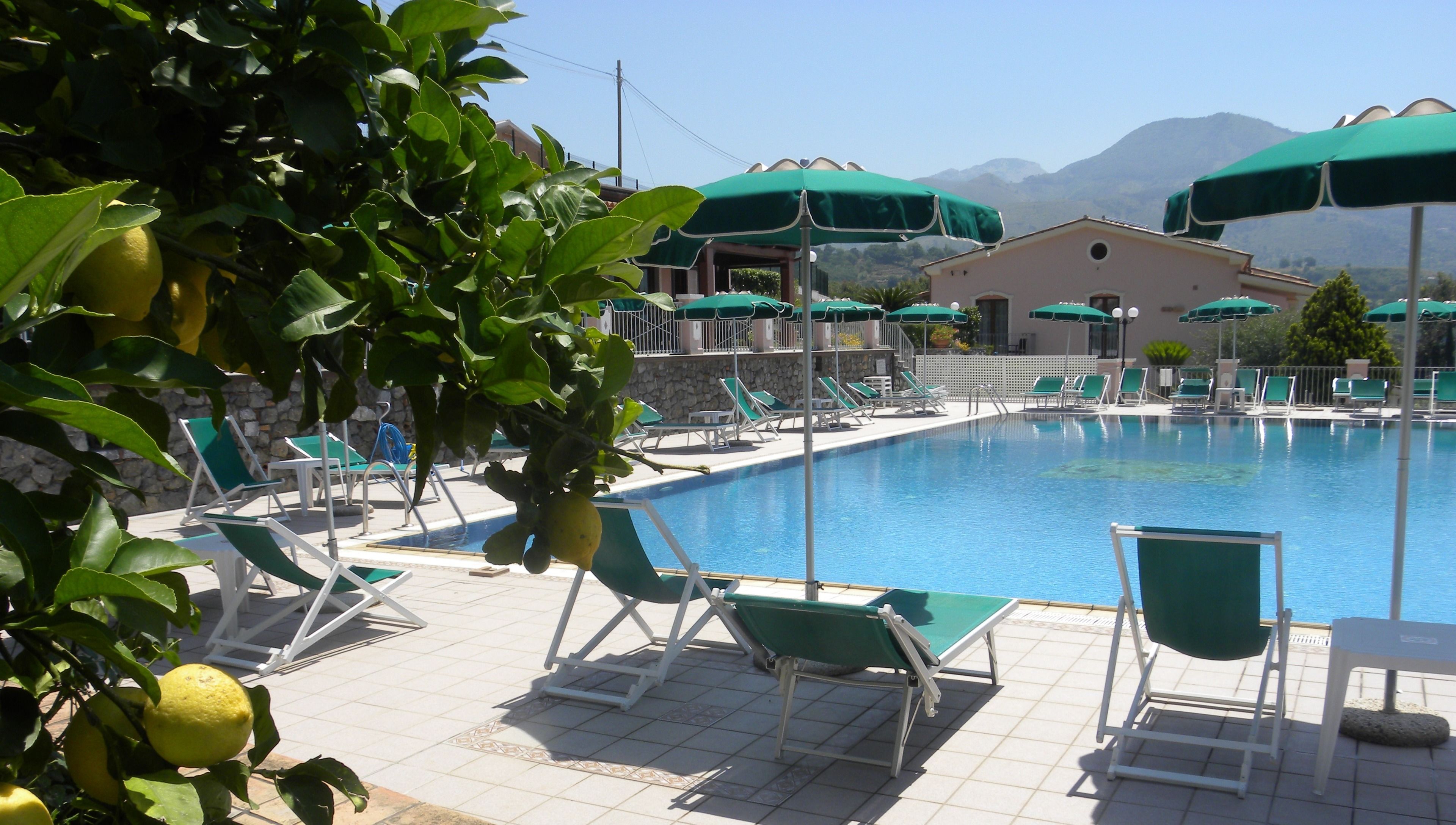 A poolside area with lounge chairs and umbrellas, a stone wall, and a mountain backdrop.