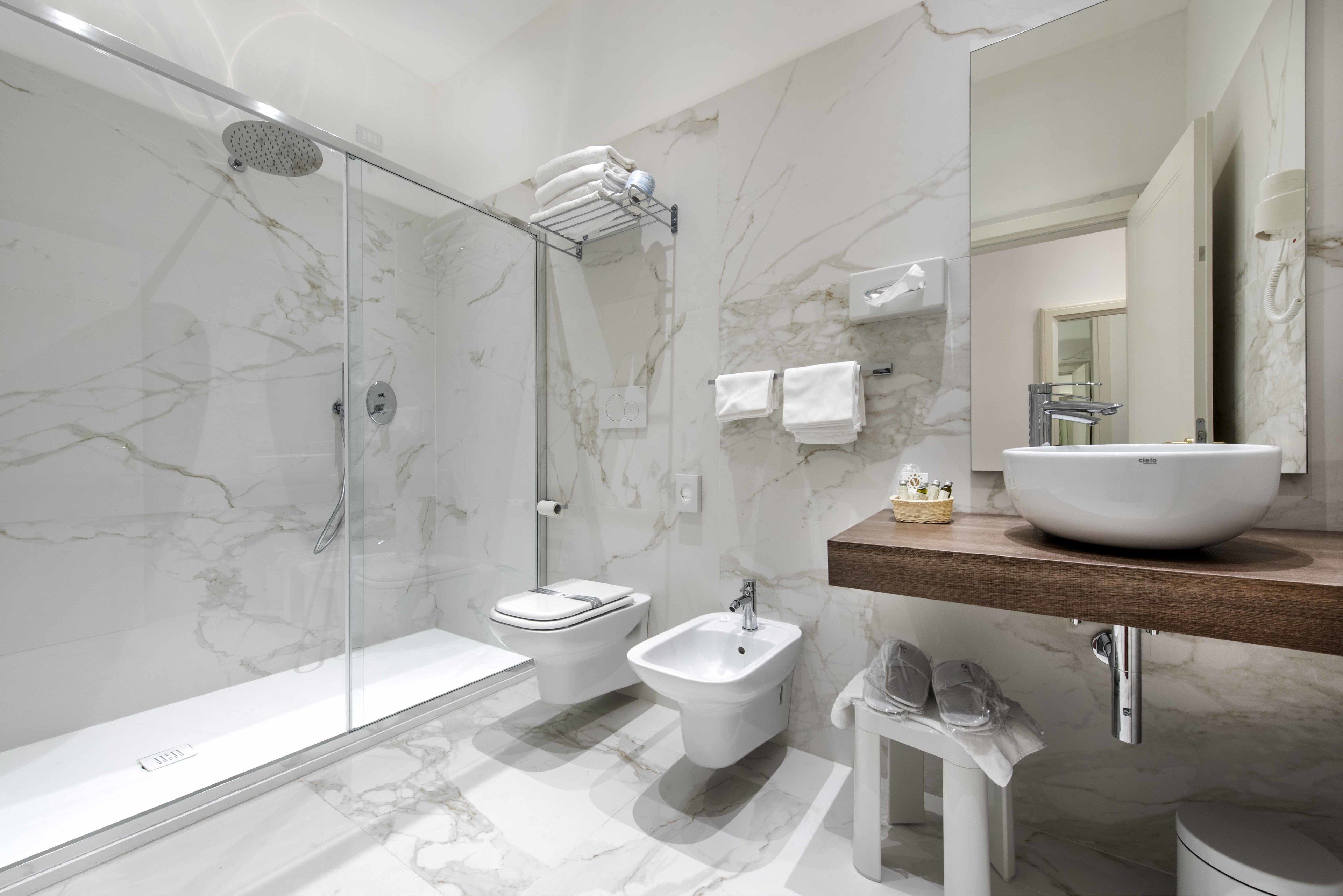A modern bathroom with a glass-enclosed shower, a bidet, a toilet, and a large sink with a marble countertop.