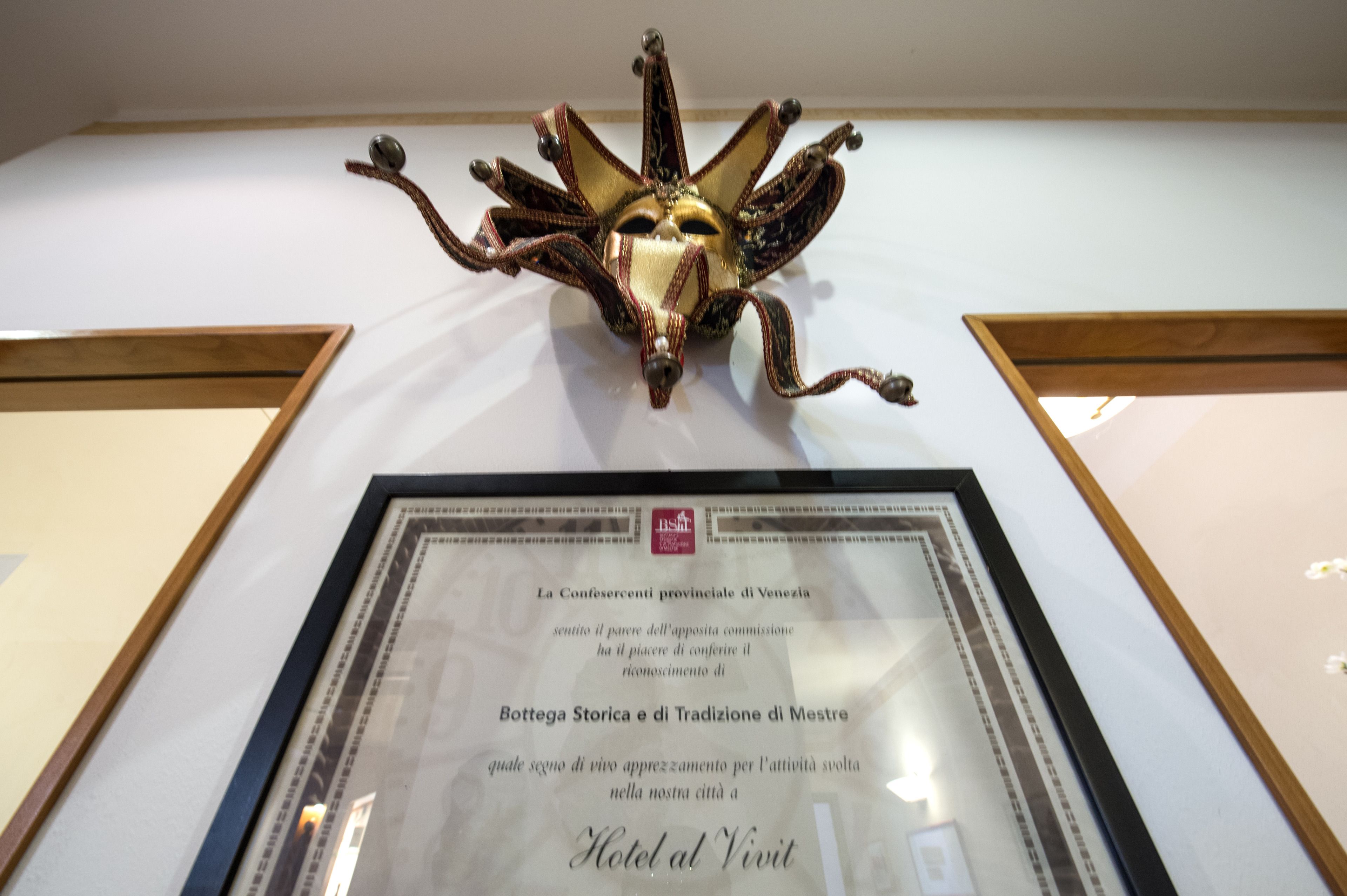 Un certificato incorniciato su una parete, con una maschera decorativa sopra.