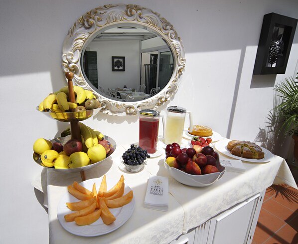 Un bufé de desayuno con diversas frutas y pasteles, un espejo y una pequeña mesa con un menú.