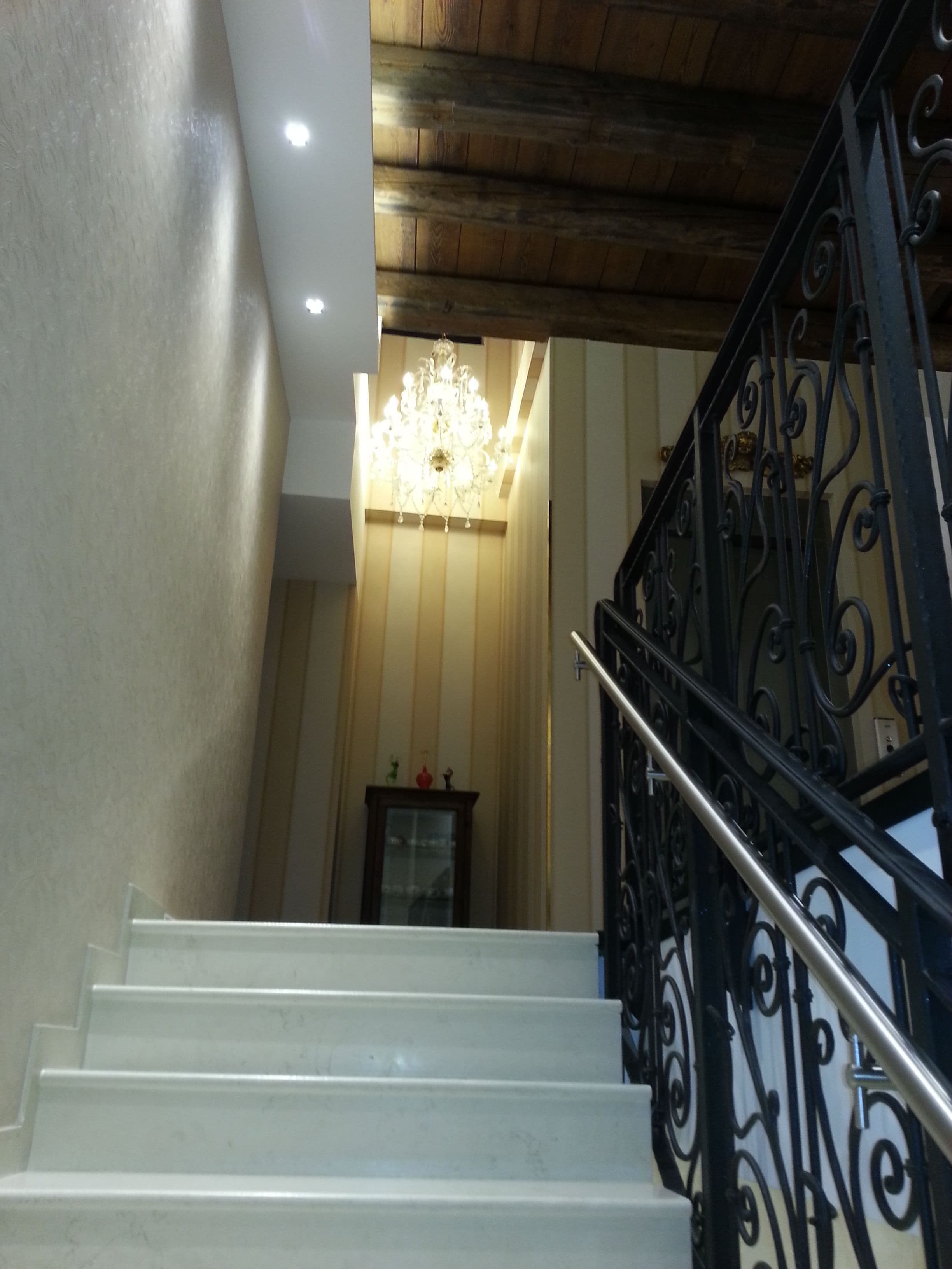 Una escalera con escalones blancos, barandilla de hierro forjado negro y un candelabro al fondo.
