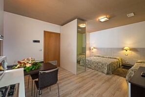 Habitación de hotel pequeña con zona de comedor, cama con ropa de cama estampada y un espejo que refleja el espacio.