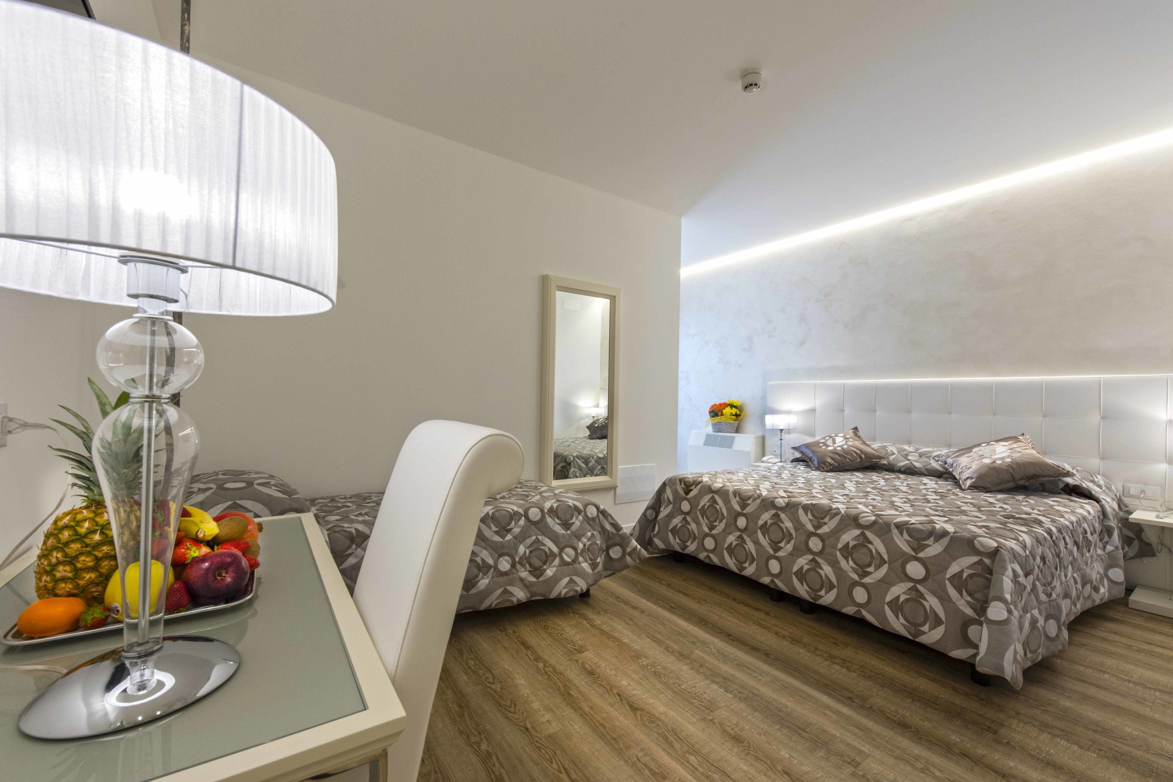 Ein modernes Hotelzimmer mit Glastisch, Obstschale und zwei Betten mit gemusterten Bettbezügen, sowie einem großen Spiegel.