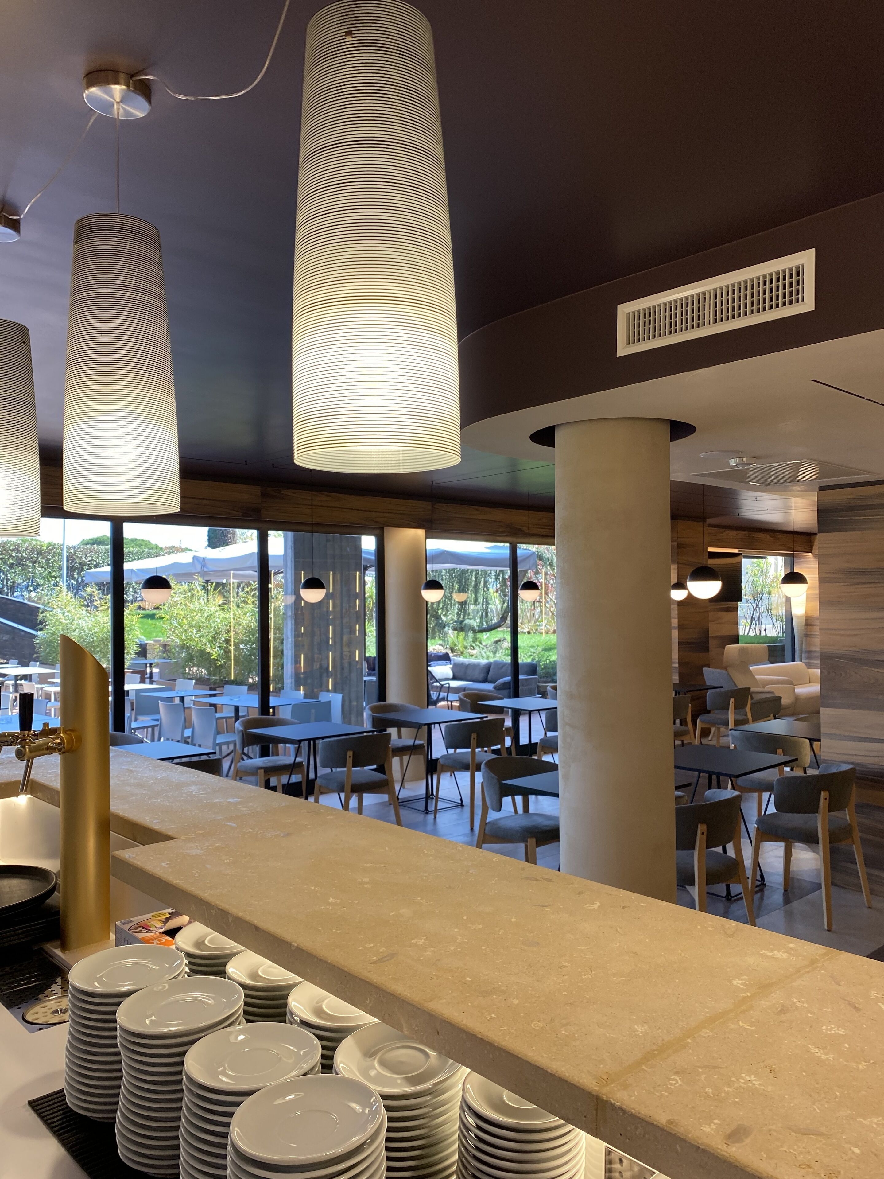 Un interior de restaurante moderno con una larga barra, varias mesas y lámparas colgantes.