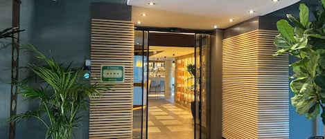 Ein Hotel mit modernem Design, das einen Empfangsbereich, eine 4-Sterne-Beschilderung und eine durch Glastüren sichtbare Bar umfasst.