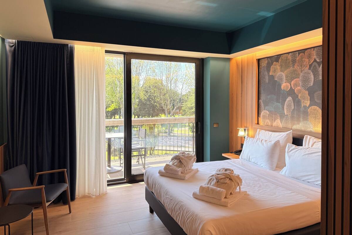 Ein Hotelzimmer mit Bett, Sessel, Tisch und Blick ins Freie durch eine Schiebetür.