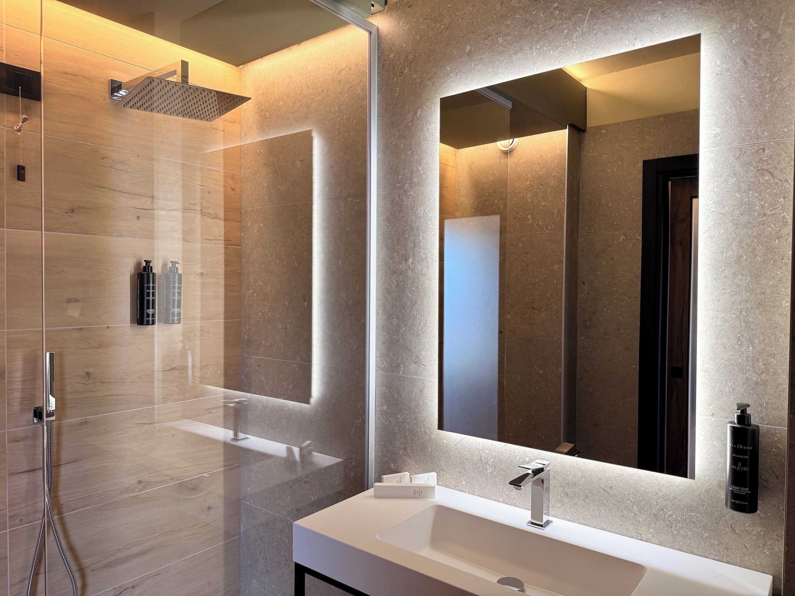 Un baño moderno con un espejo grande, ducha y lavamanos.