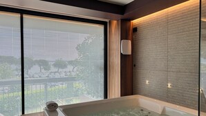 Un baño moderno con bañera de hidromasaje de vidrio, ventanas amplias y un mueble de tocador de madera.