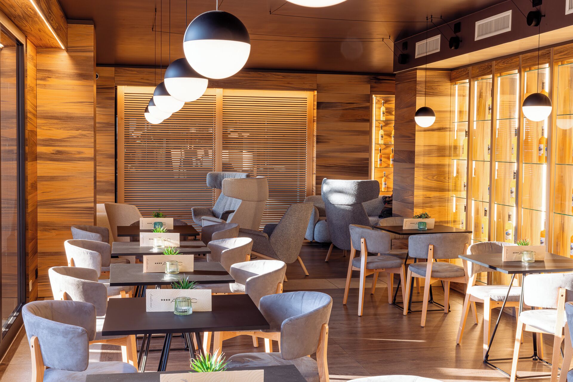 A modern interior with wooden panel walls, multiple seating areas, and pendant lighting.