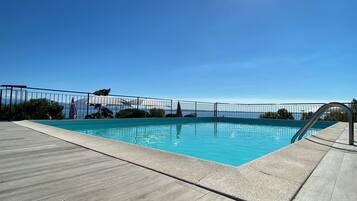 A clear blue sky, a swimming pool with a metal railing, and a view of the sea.