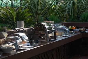 Montaje de bufé con diferentes alimentos y una máquina de café, rodeado de abundante vegetación.