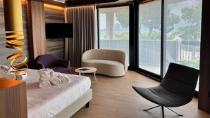 Una habitación de hotel moderna con una cama grande, dos sillones, una mesita y un televisor.