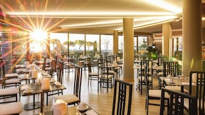 Un restaurante espacioso con varias mesas y sillas, ventanas amplias que ofrecen vistas al exterior y una decoración de diseño moderno.