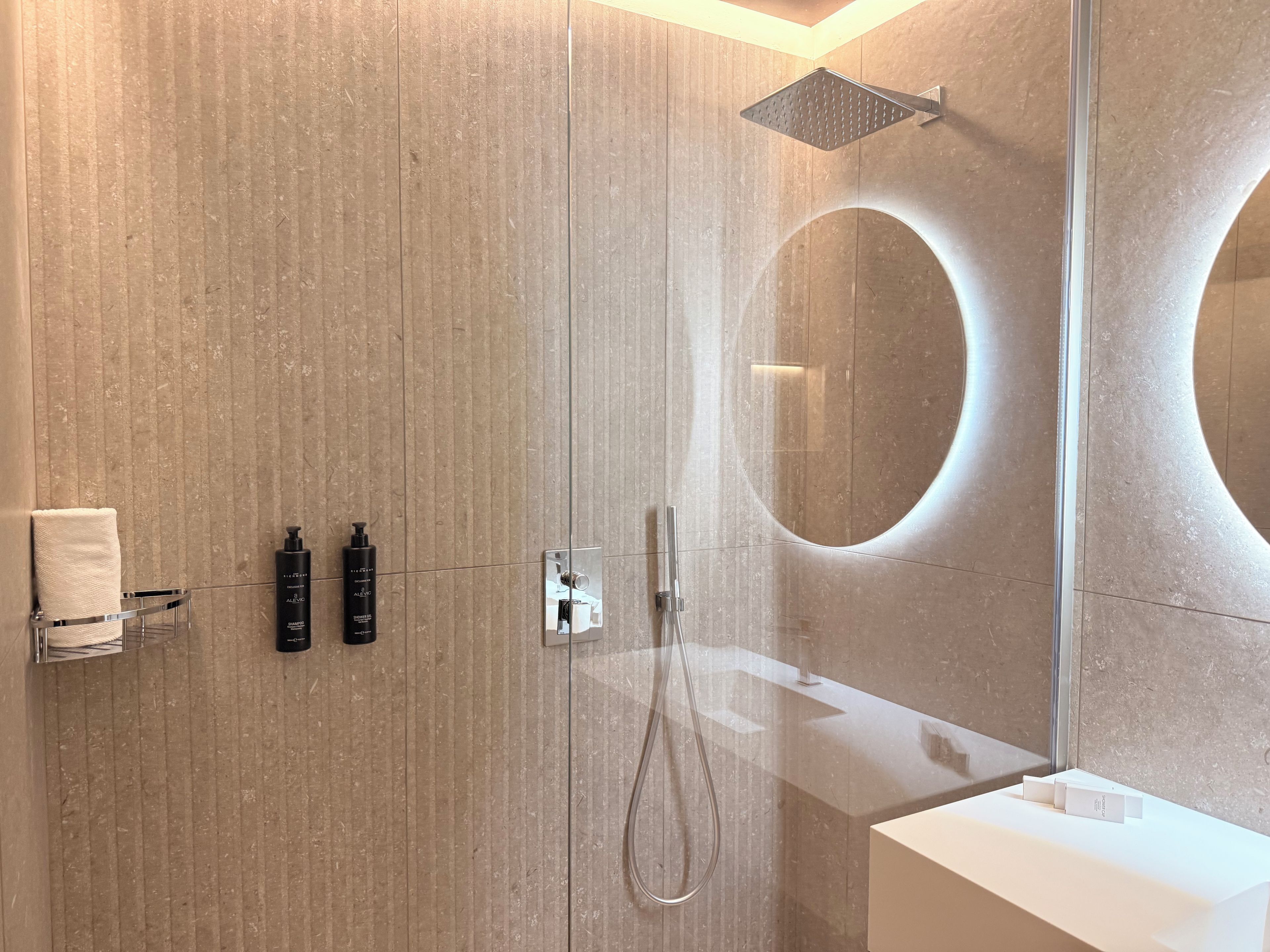 Un bagno moderno con un ampio specchio, una doccia e un piano d'appoggio bianco.