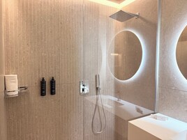 Un bagno moderno con un ampio specchio, una doccia e un piano d'appoggio bianco.