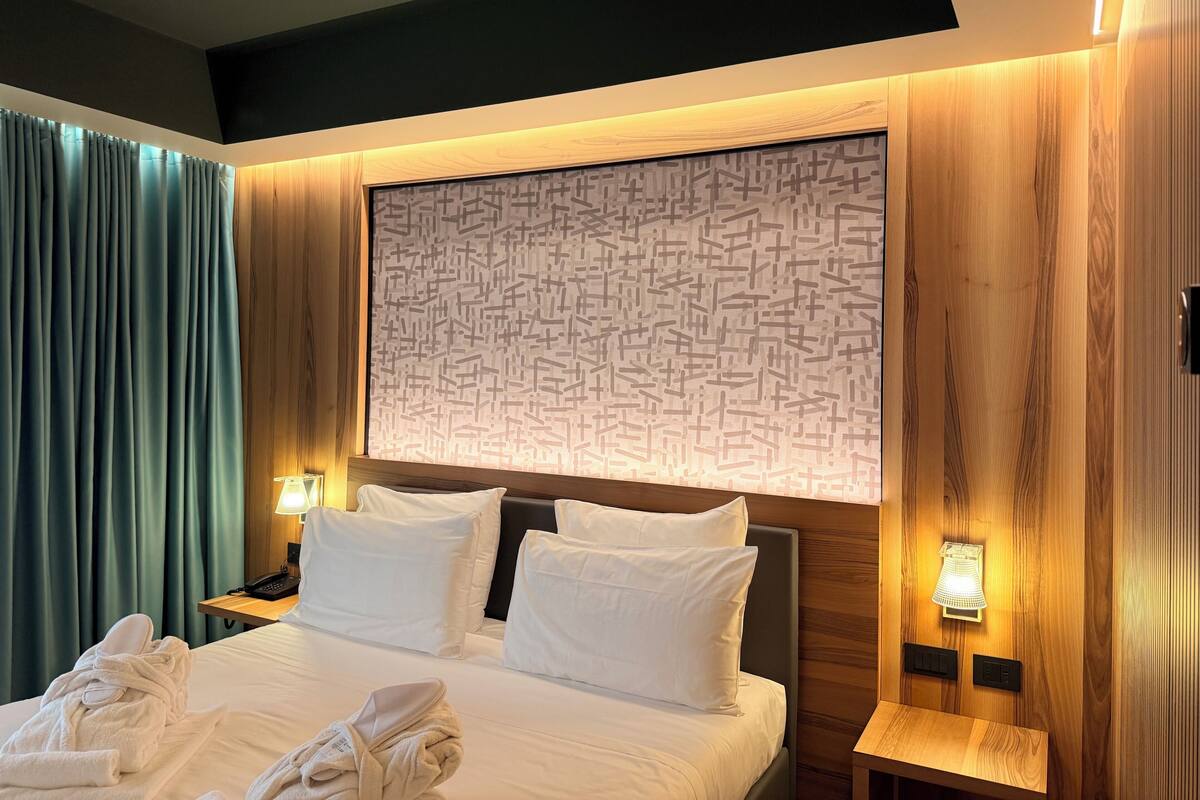 Ein Hotelzimmer mit einem großen Bett, zwei Nachttischen, einer Wandleuchte und einem gemusterten Kopfteil.