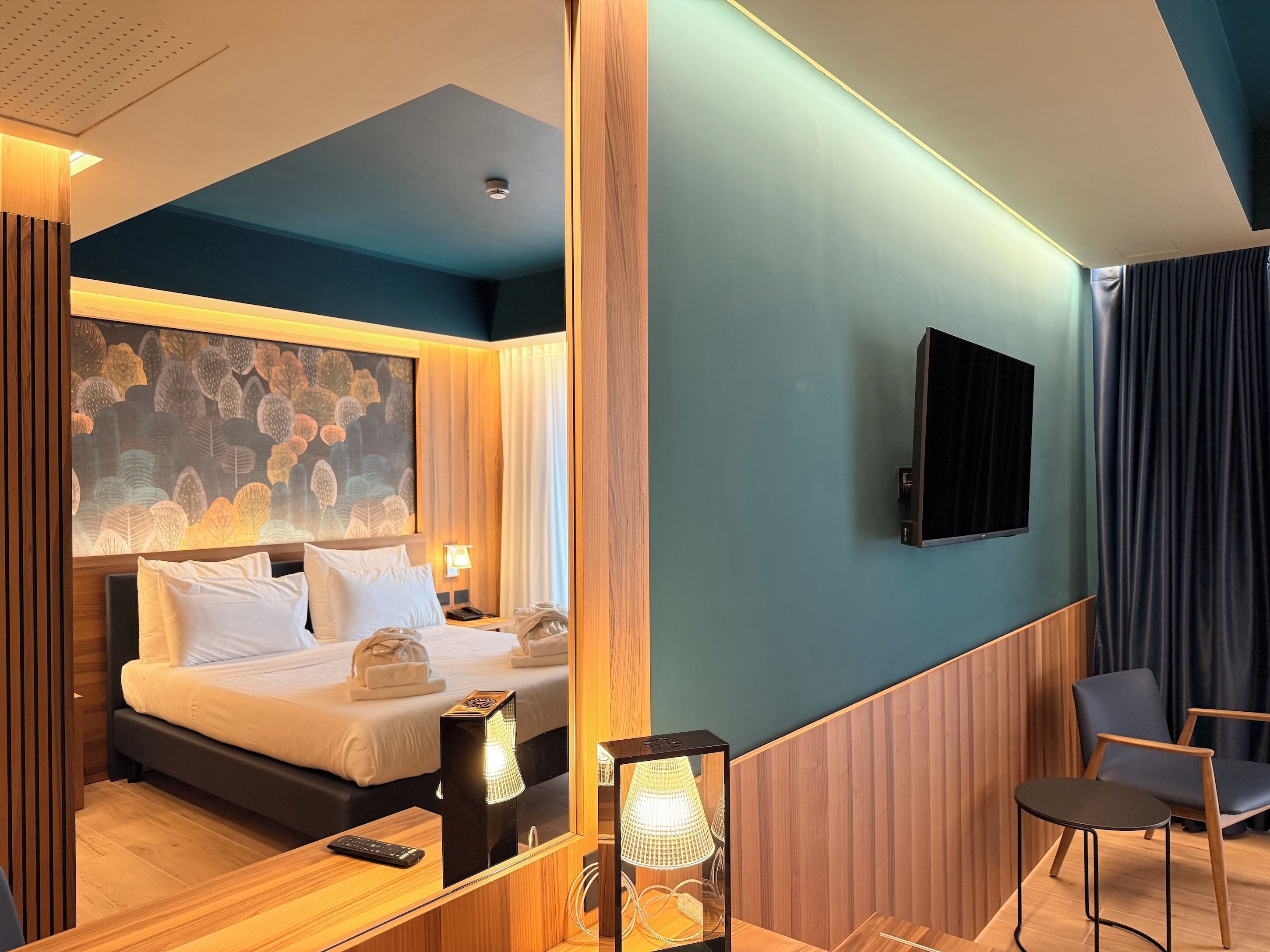 A hotel room with a bed, bedside table, lamp, TV, and a chair.